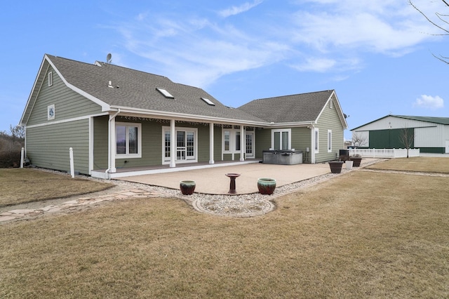 rear view of house featuring a hot tub, roof with shingles, a lawn, and a patio