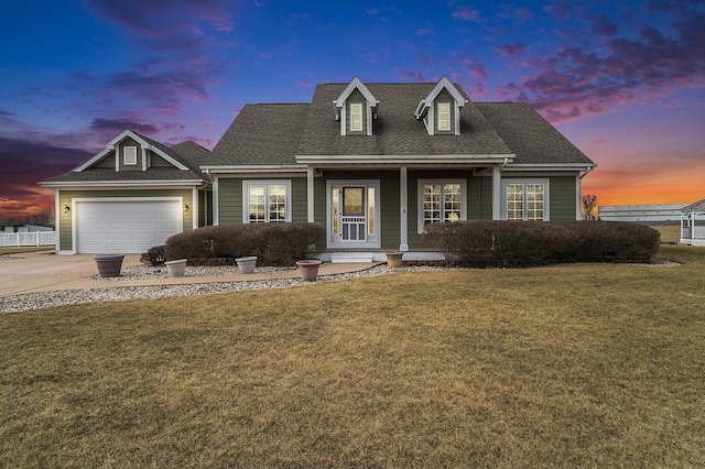 cape cod-style house featuring driveway, roof with shingles, a garage, and a yard