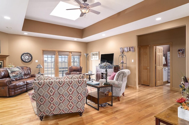 living room featuring a glass covered fireplace, light wood finished floors, and a tray ceiling