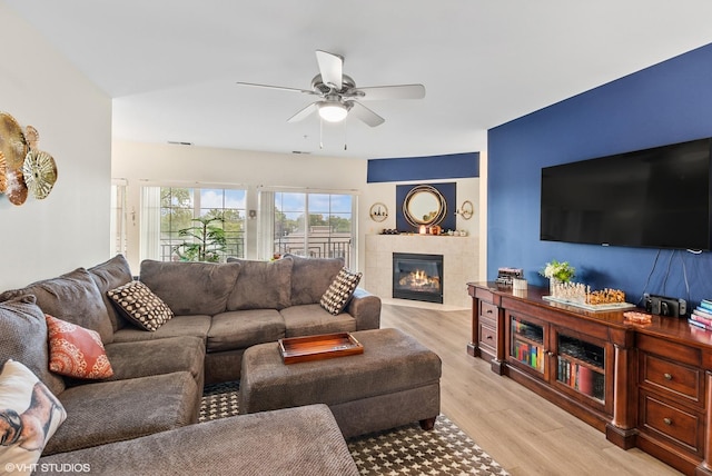 living room featuring light wood-style floors, a tile fireplace, visible vents, and a ceiling fan