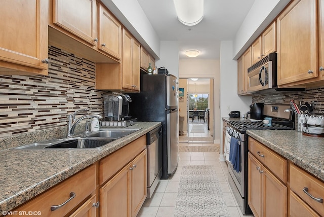 kitchen with light tile patterned floors, a sink, appliances with stainless steel finishes, tasteful backsplash, and dark countertops