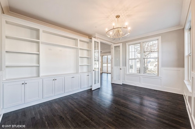 interior space with dark wood-style flooring, crown molding, a decorative wall, wainscoting, and a chandelier