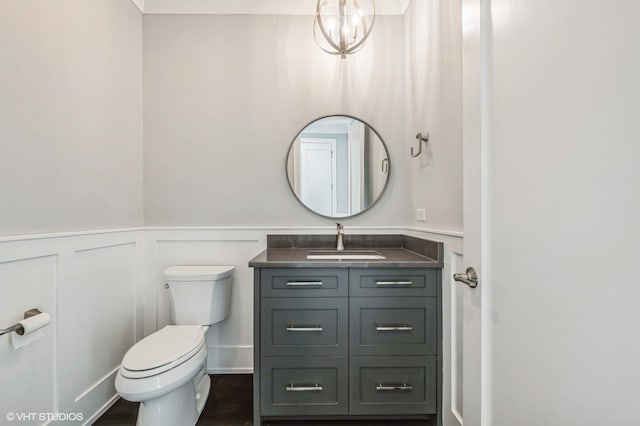 half bathroom with wainscoting, toilet, wood finished floors, vanity, and a decorative wall