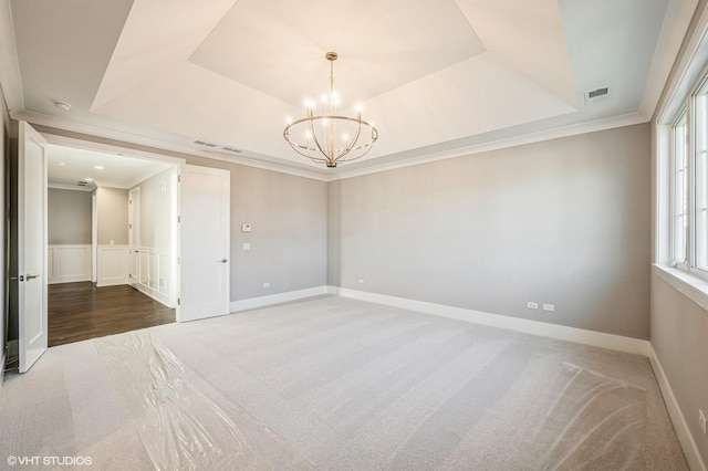 carpeted empty room featuring ornamental molding, a tray ceiling, a chandelier, and visible vents