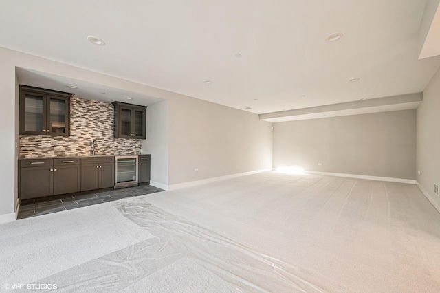 unfurnished living room with beverage cooler, light carpet, indoor wet bar, and baseboards