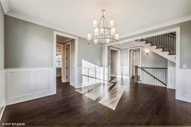 spare room featuring ornamental molding, a decorative wall, wood finished floors, and an inviting chandelier
