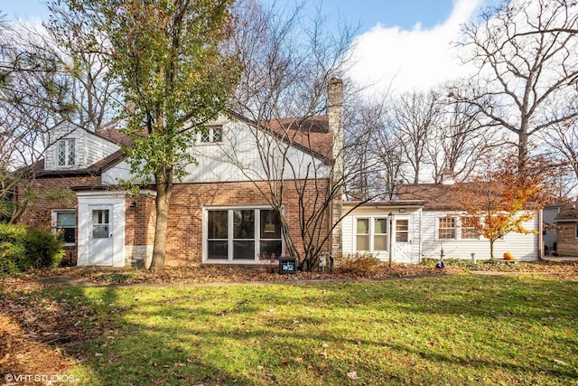 back of property featuring brick siding, a lawn, and a chimney