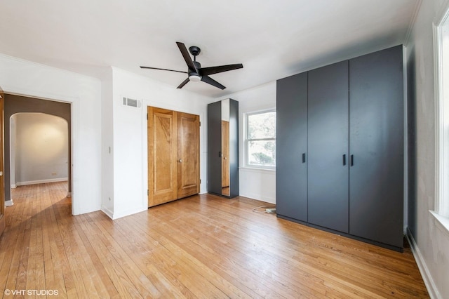 unfurnished bedroom with arched walkways, visible vents, light wood-style flooring, and baseboards