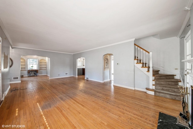 unfurnished living room featuring baseboards, arched walkways, hardwood / wood-style flooring, ornamental molding, and stairs