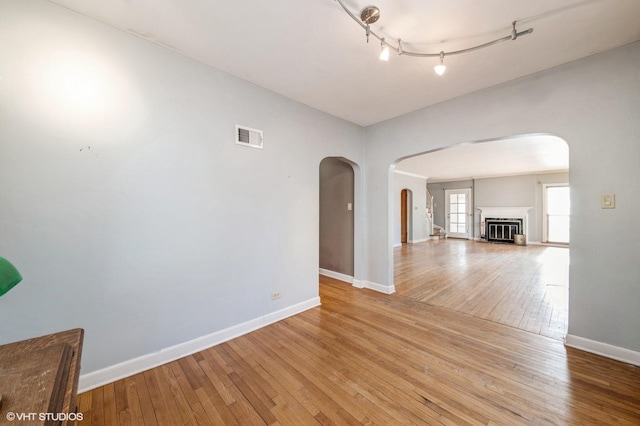 unfurnished room featuring arched walkways, baseboards, visible vents, and light wood-style floors