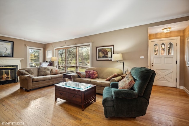 living room featuring baseboards, light wood-type flooring, a glass covered fireplace, and crown molding