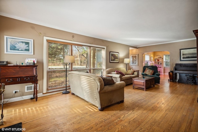 living room featuring arched walkways, crown molding, visible vents, hardwood / wood-style floors, and baseboards