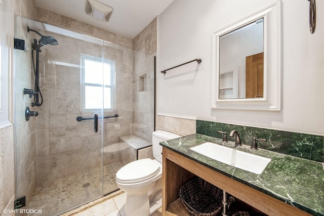 bathroom with toilet, vanity, tile walls, wainscoting, and a shower stall