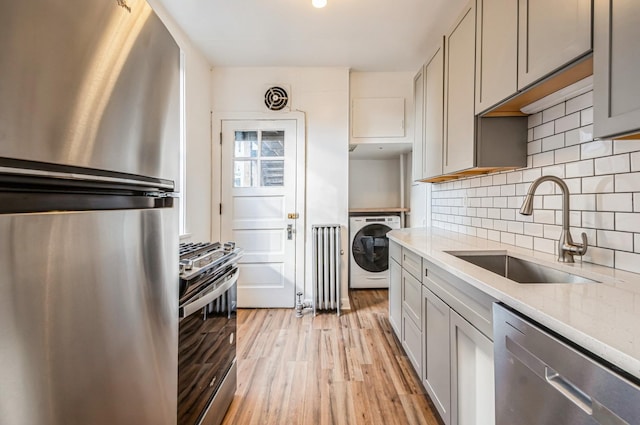 kitchen featuring stainless steel appliances, washer / clothes dryer, gray cabinetry, a sink, and light stone countertops