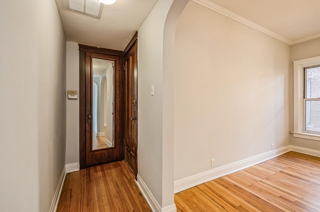 hall with baseboards, visible vents, arched walkways, wood finished floors, and crown molding