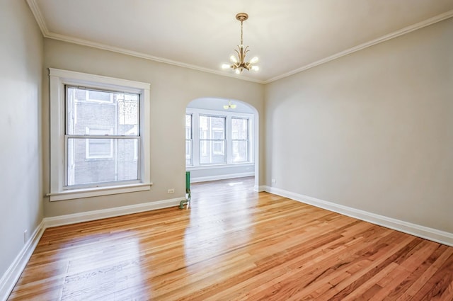 spare room featuring ornamental molding, light wood-type flooring, baseboards, and an inviting chandelier