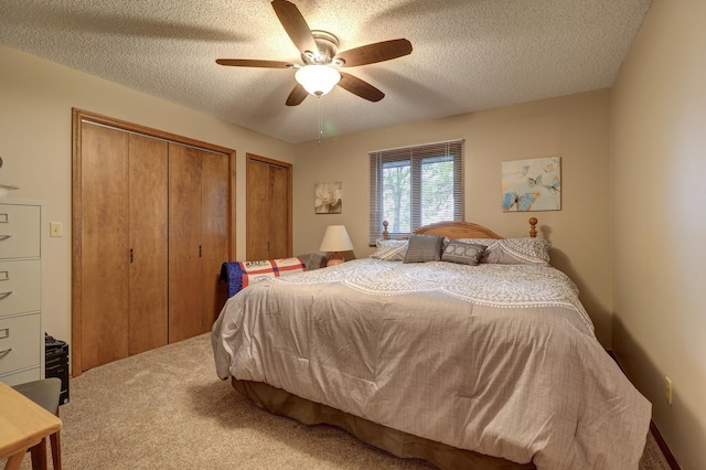 carpeted bedroom with ceiling fan, a textured ceiling, and multiple closets