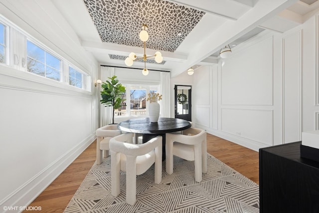 dining area with a chandelier, a decorative wall, baseboards, light wood-style floors, and beam ceiling