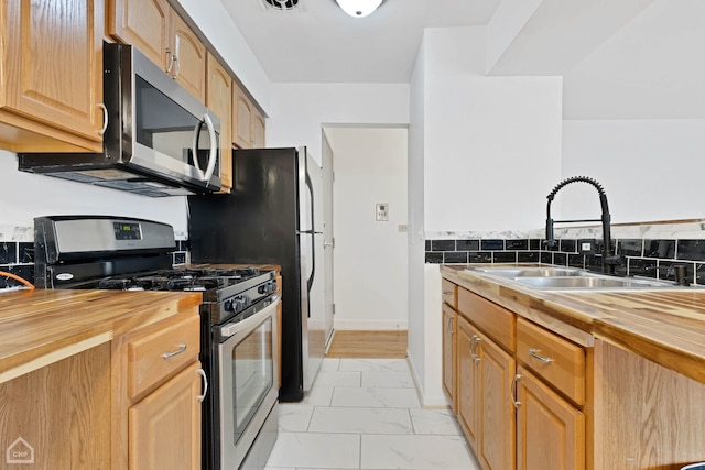 kitchen featuring baseboards, wood counters, appliances with stainless steel finishes, marble finish floor, and a sink