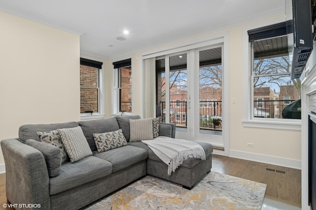 living area with ornamental molding, visible vents, baseboards, and wood finished floors