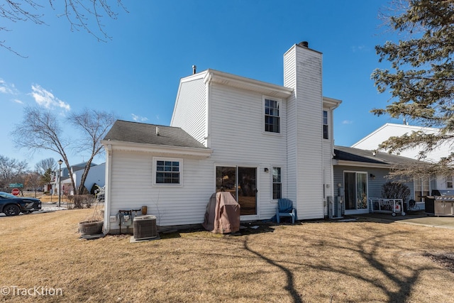 back of property with a lawn, a chimney, and central air condition unit