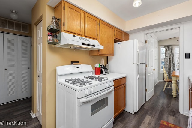 kitchen with white appliances, visible vents, dark wood-type flooring, light countertops, and under cabinet range hood