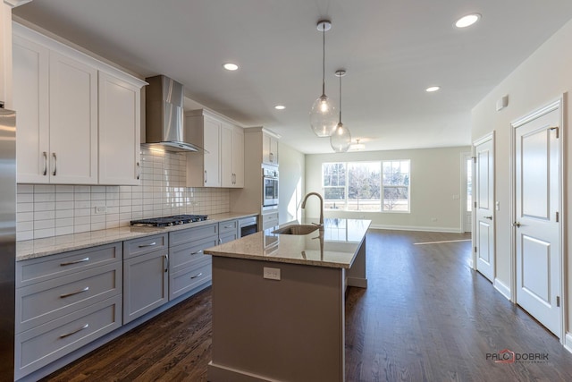 kitchen featuring a kitchen island with sink, stainless steel appliances, a sink, wall chimney range hood, and tasteful backsplash