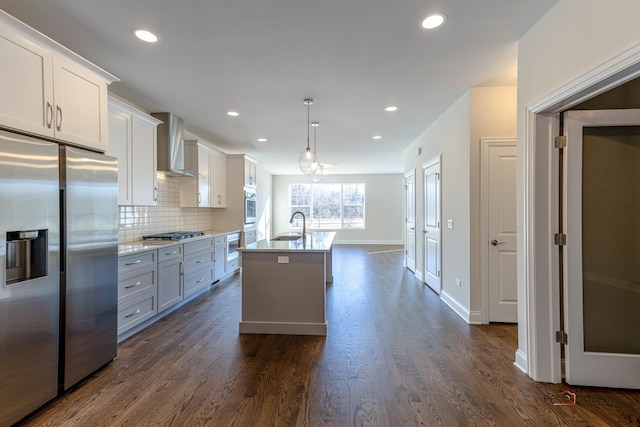 kitchen with dark wood-style floors, a center island with sink, appliances with stainless steel finishes, a sink, and wall chimney exhaust hood