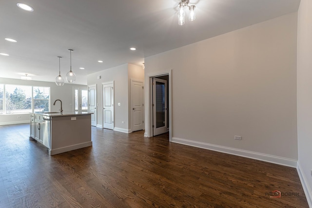 kitchen featuring dark wood-style floors, a center island with sink, open floor plan, a sink, and baseboards