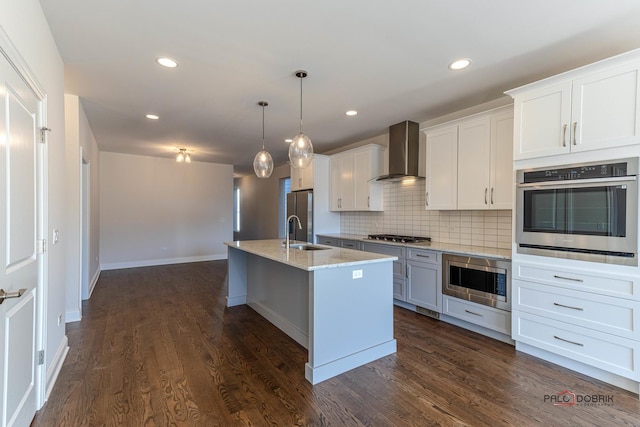 kitchen with dark wood-style floors, stainless steel appliances, wall chimney exhaust hood, and a sink