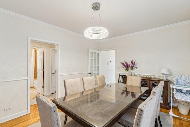 dining area with ornamental molding, a notable chandelier, light wood-style flooring, and baseboards