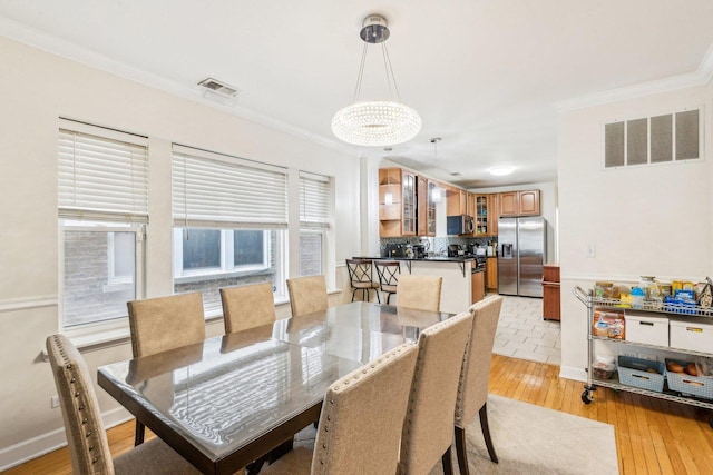 dining room with light wood-style floors, a notable chandelier, visible vents, and crown molding