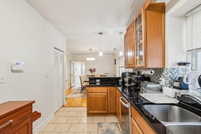 kitchen with a peninsula, a sink, brown cabinets, tasteful backsplash, and glass insert cabinets