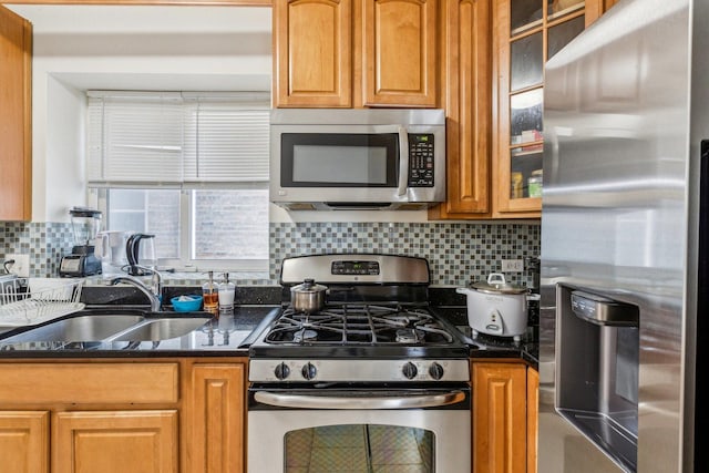 kitchen with stainless steel appliances, backsplash, brown cabinetry, glass insert cabinets, and a sink