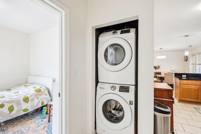 clothes washing area with stacked washer and clothes dryer, light tile patterned floors, and laundry area