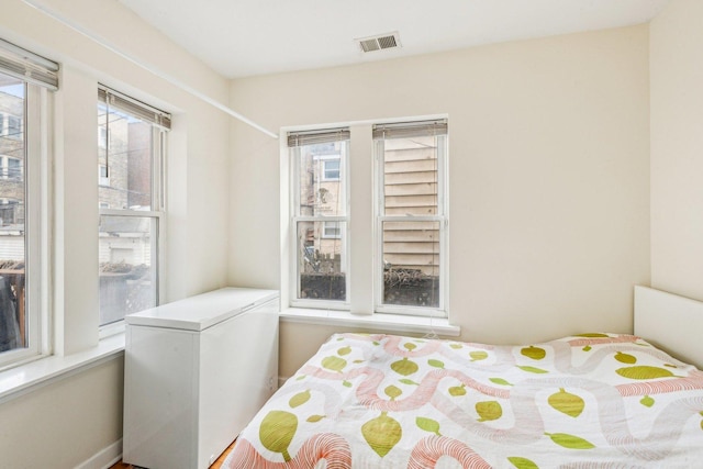 bedroom with multiple windows, fridge, and visible vents