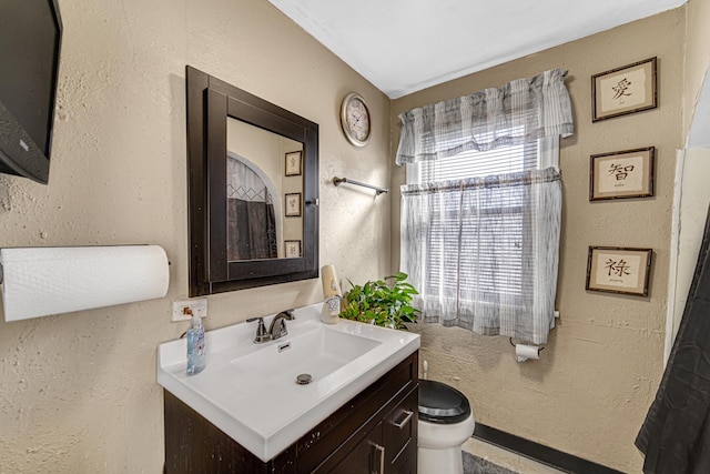 bathroom with toilet, a textured wall, and vanity