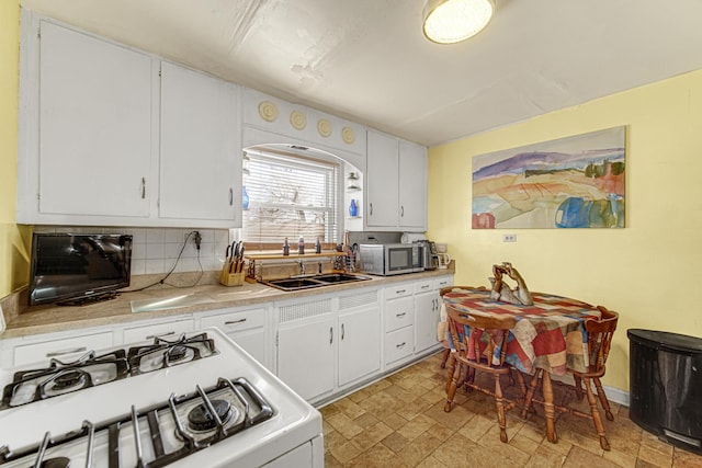 kitchen with a sink, white range with gas cooktop, white cabinets, light countertops, and stainless steel microwave