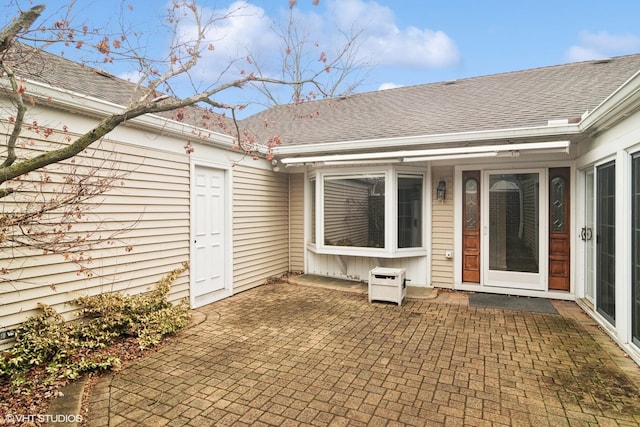 entrance to property with a shingled roof and a patio area