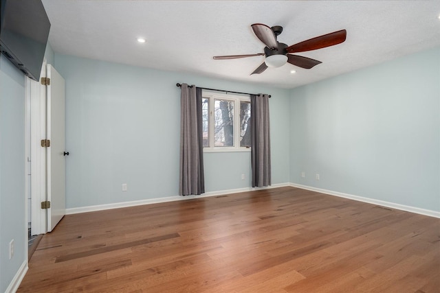 empty room featuring a ceiling fan, recessed lighting, baseboards, and wood finished floors