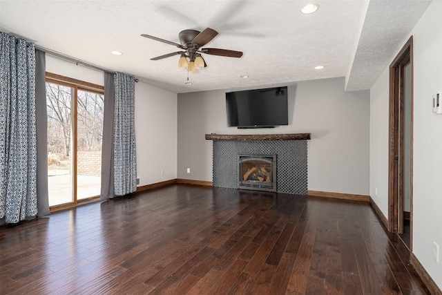 unfurnished living room featuring baseboards, a textured ceiling, a tiled fireplace, and wood finished floors