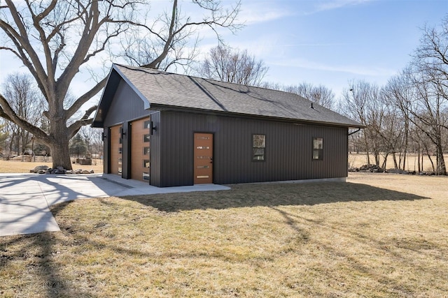 view of side of home with a garage, roof with shingles, an outbuilding, and a yard