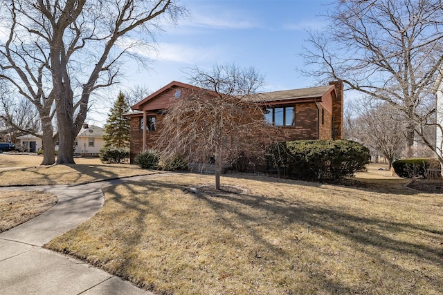 view of front of home featuring a chimney, a front lawn, and brick siding