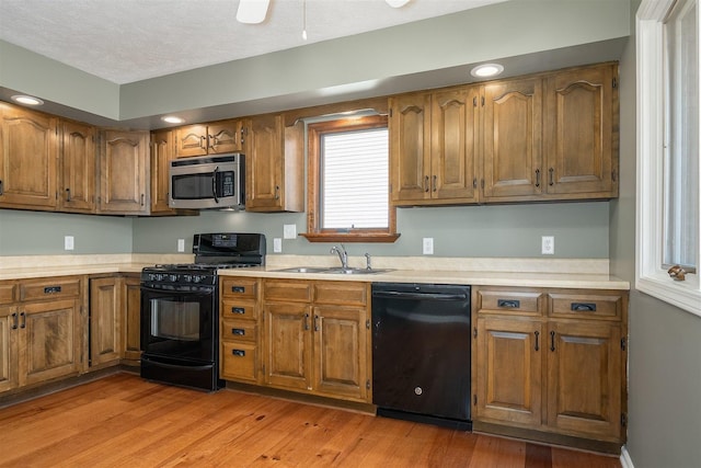 kitchen featuring a sink, light countertops, light wood-type flooring, brown cabinets, and black appliances