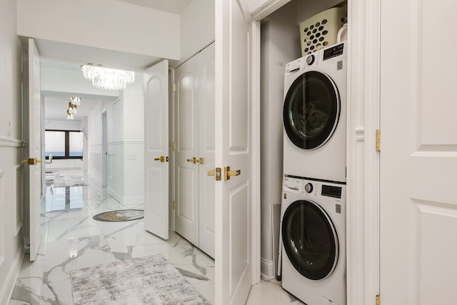 laundry area featuring marble finish floor, stacked washer and clothes dryer, a chandelier, and laundry area