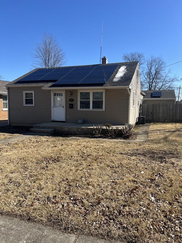 ranch-style house featuring a chimney, fence, central AC unit, and solar panels