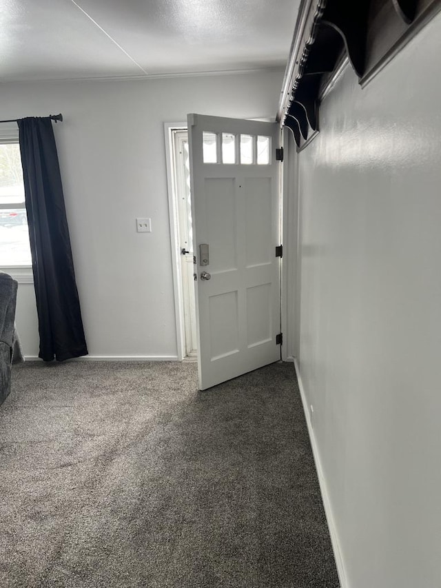 entryway featuring baseboards, dark colored carpet, and a textured ceiling