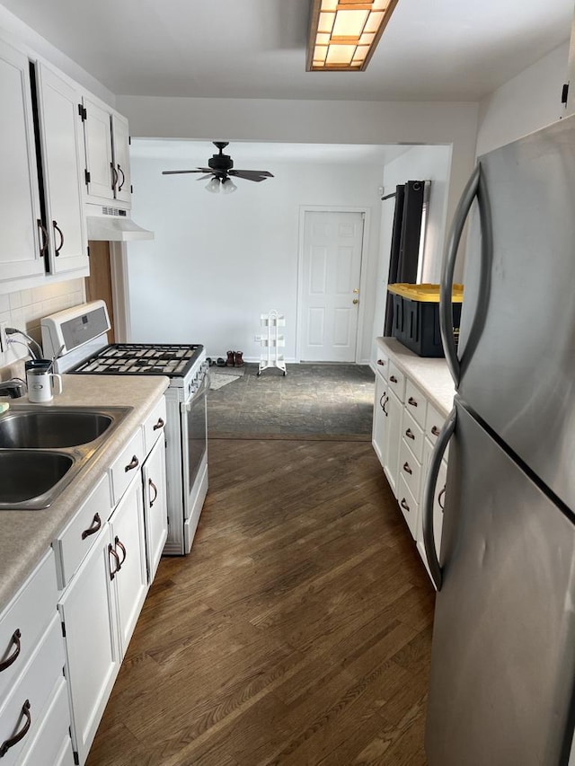 kitchen with white gas stove, white cabinets, light countertops, freestanding refrigerator, and dark wood-style floors