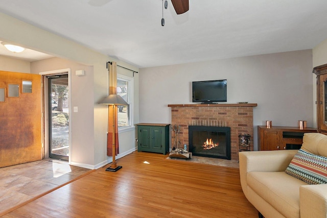 living room with light wood-type flooring, baseboards, a brick fireplace, and a ceiling fan