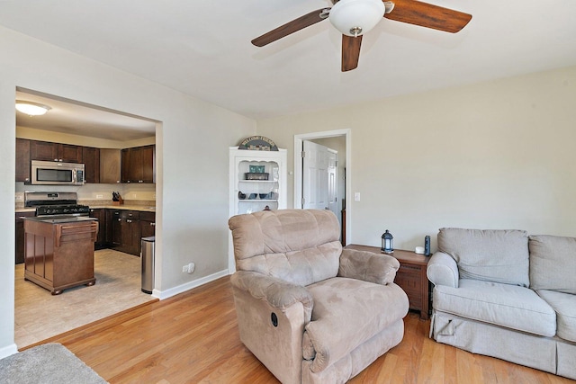 living area featuring baseboards, ceiling fan, and light wood finished floors